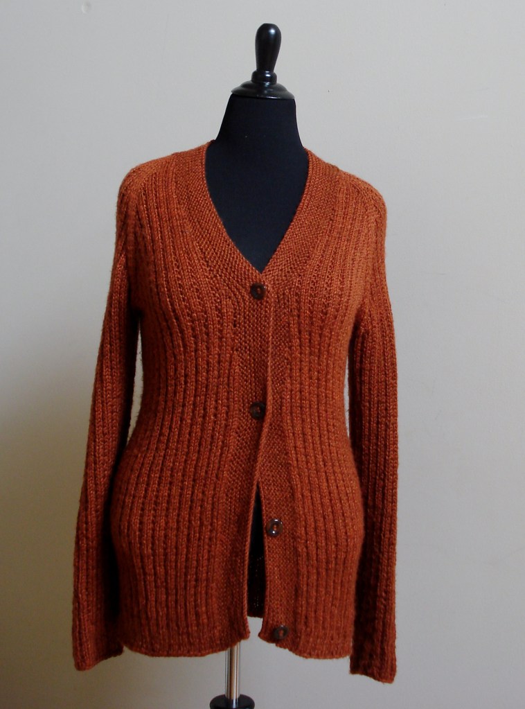 An orange knitted cardigan displayed on a dress form, featuring a V-neck, long sleeves, and three buttons down the front.
