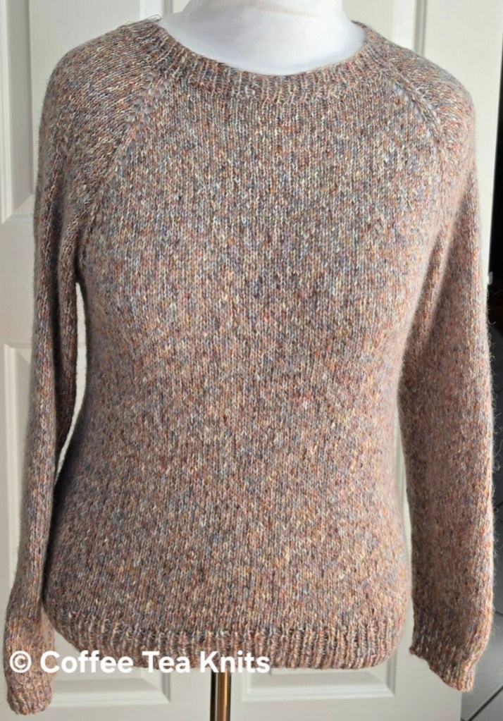 Close-up of a hand-knitted sweater displayed on a mannequin, showcasing a textured knit design in warm colors.